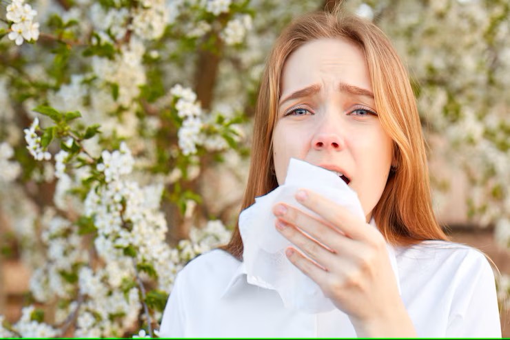 Kobieta kichająca wśród kwitnących drzew – alergia na pyłki wiosną