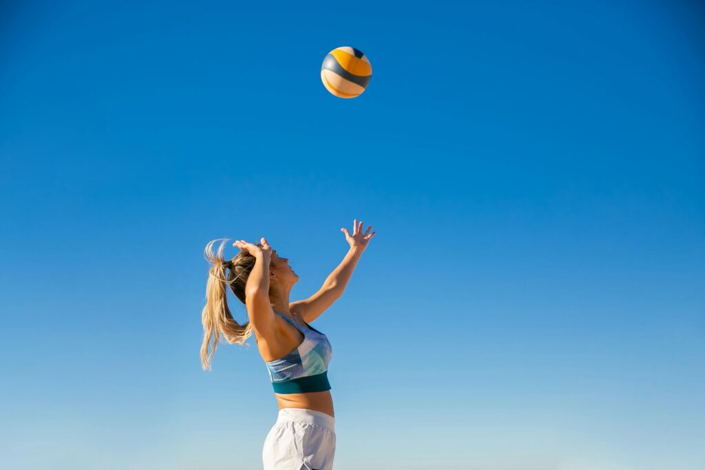 A woman spiking a volleyball on the beach under a clear blue sky, showcasing athletic skill and summer fun.