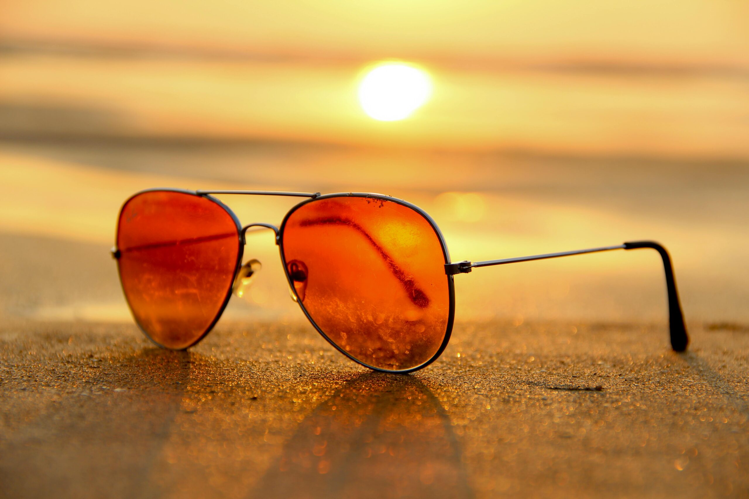 Close-up of sunglasses on a beach during a vibrant sunset, capturing the essence of summer. suplementy diety na lato