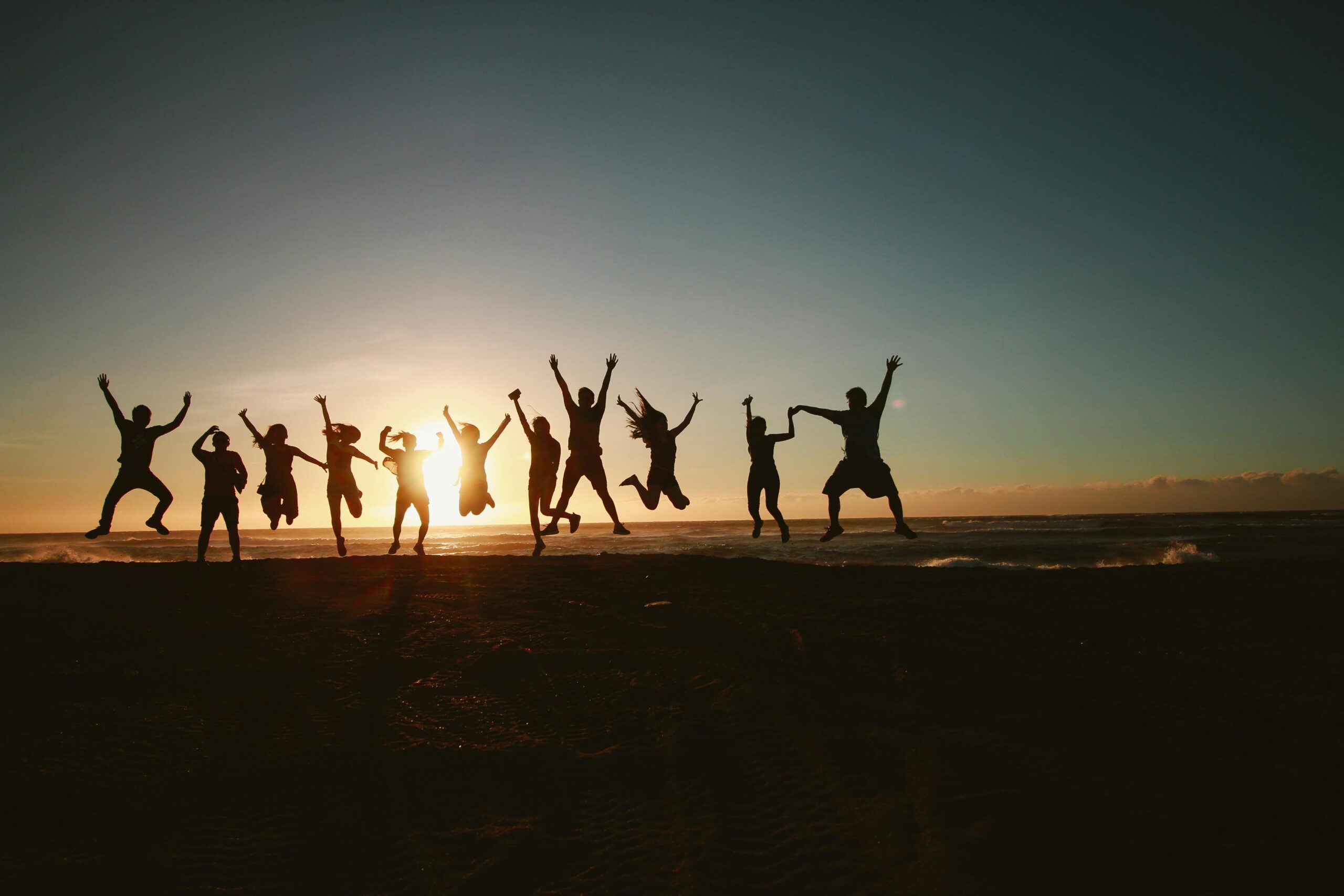 relacje międzyludzkie Silhouette of a group of friends jumping on a beach at sunset, expressing joy and freedom.