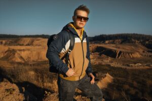 A young man standing outdoors in casual attire enjoying a sunny day.
